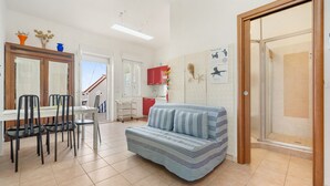A living room with a sofa, dining table, chairs, and a kitchen area with cabinets and a red cabinet. - Casa Susanna – Your Retreat in Calasetta: Sea, Culture, and Relaxation (Calasetta)