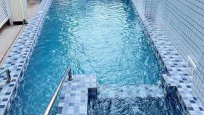 Ein rechteckiger Pool mit gefliestem Rand, einer Metallleiter und einer Rutsche.