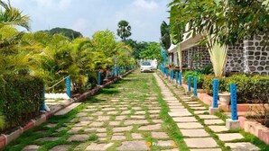 A pathway leading to a building with a stone wall and blue bollards. - Kakatiya Resort (Govindaraopet)