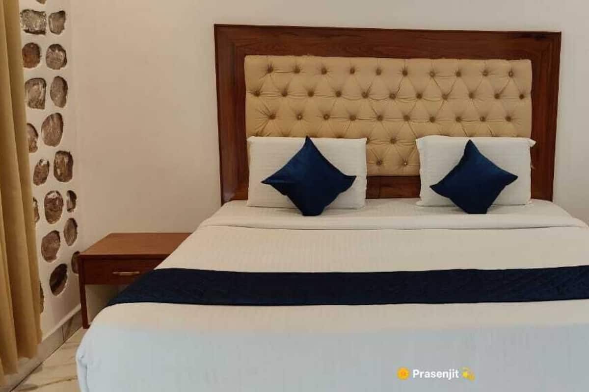 Un dormitorio con cabecera capitonada, dos almohadas, una colcha y una mesita de noche.