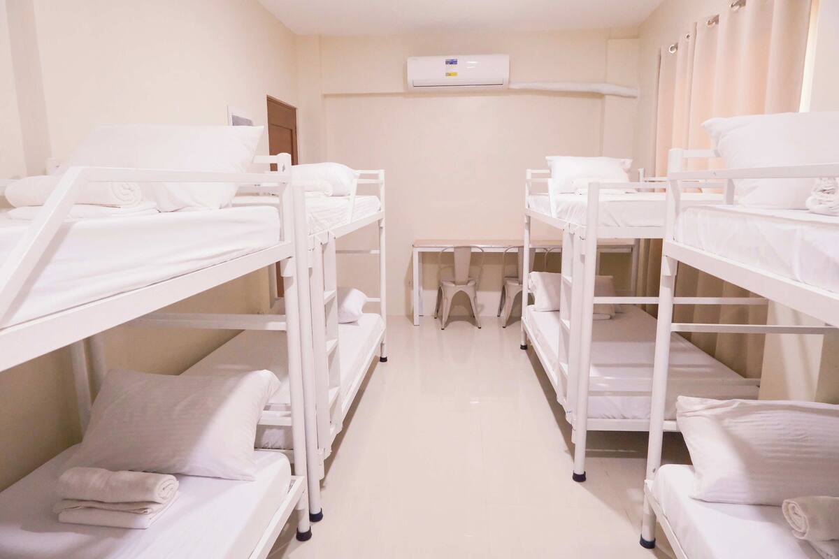 A hotel room with bunk beds, a small table, and an air conditioning unit.