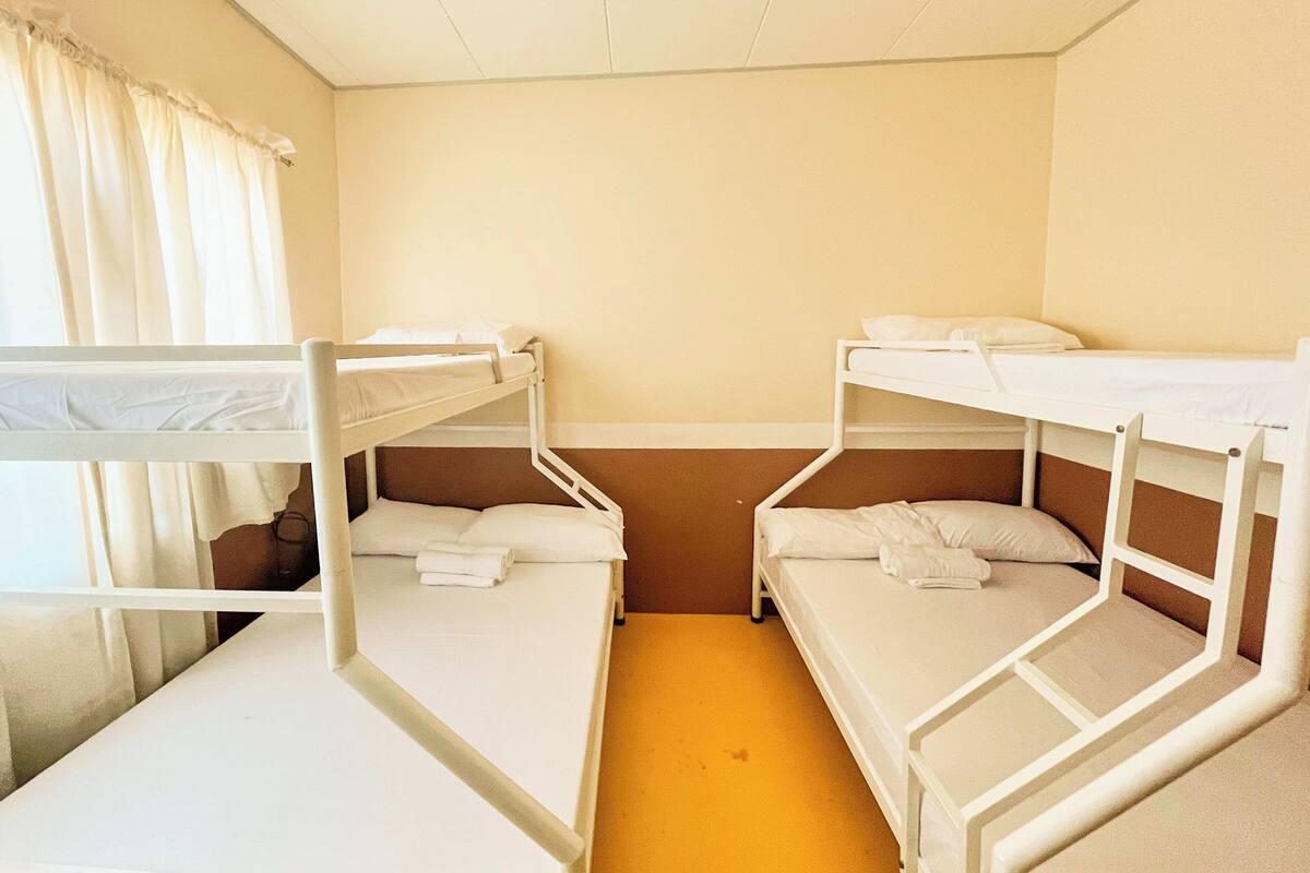 A room with bunk beds, a window with curtains, and a plain wall.