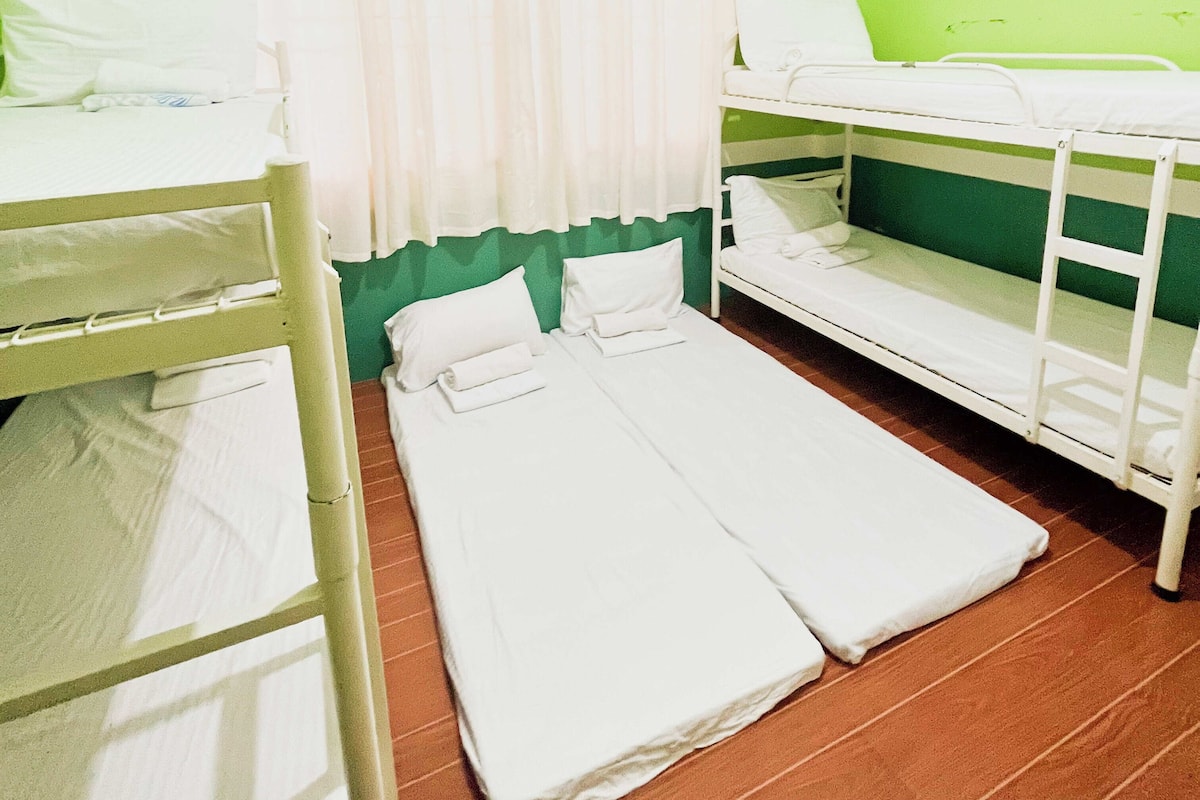 A room with bunk beds and a single bed, wooden flooring, and a green wall.