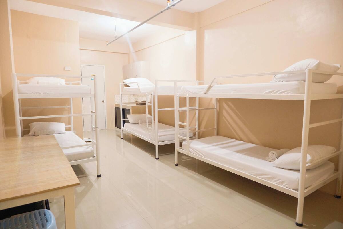 A dormitory room with bunk beds, a desk, and a chair.