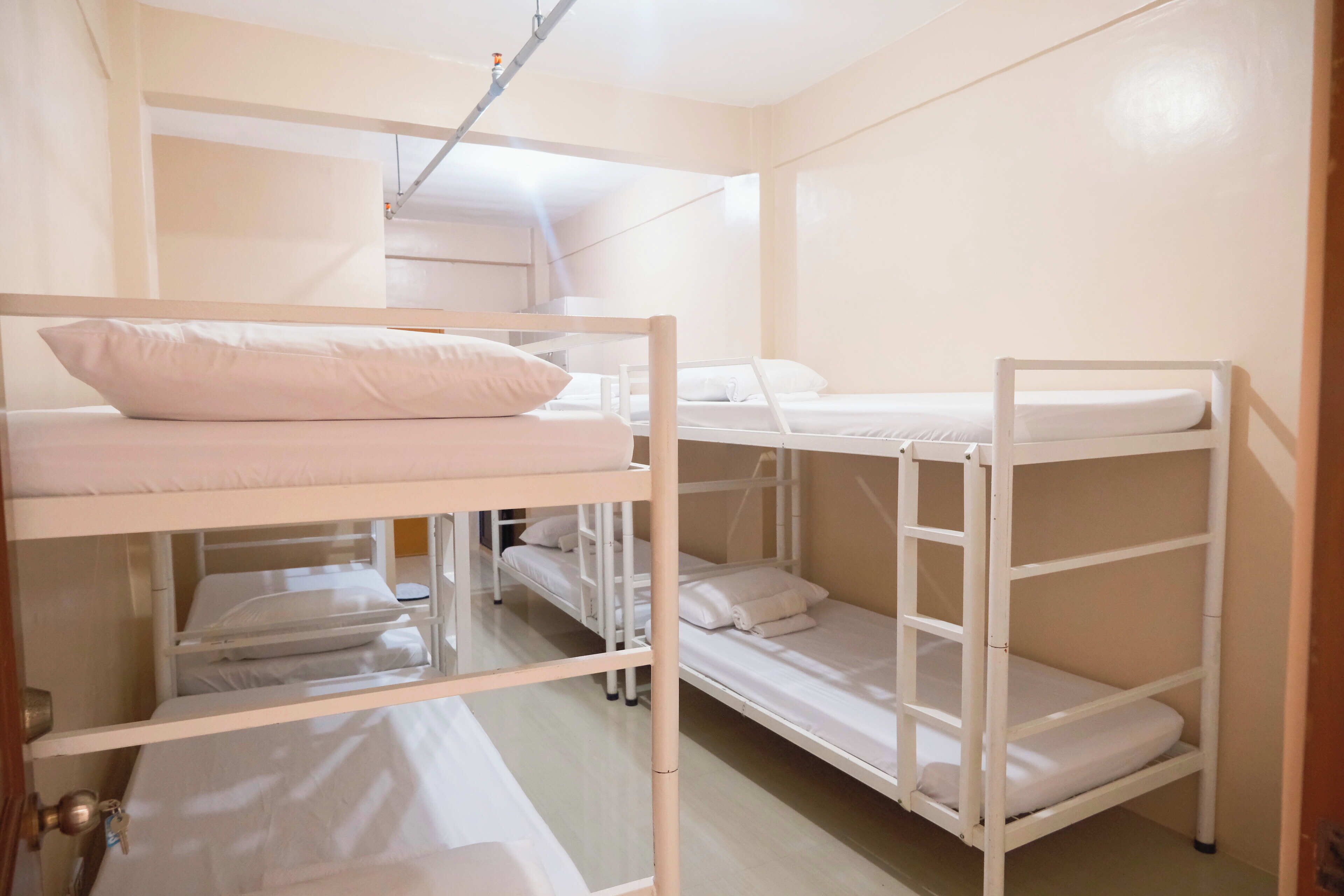 Dormitorio con literas, ropa de cama blanca y estructura metálica.