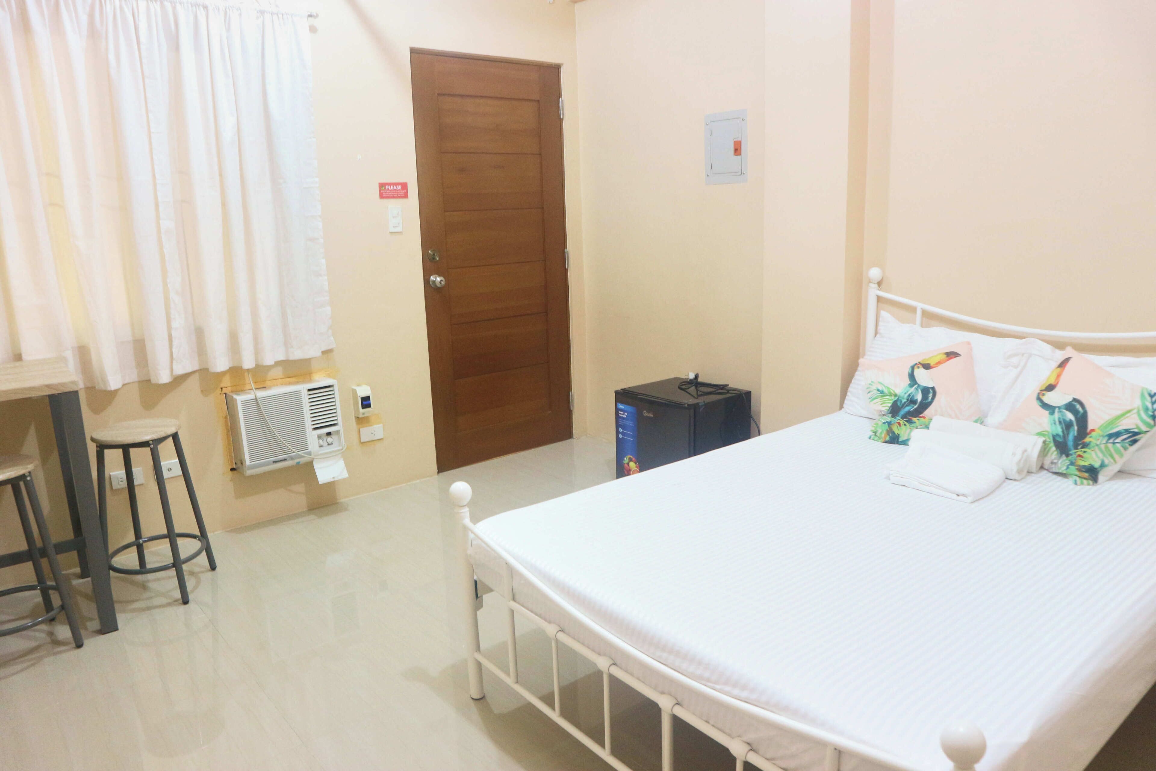A bedroom with a bed, a wooden door, a radiator, and a stool.