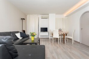 Un soggiorno moderno con un divano nero, un piccolo tavolino, una TV, un tavolo da pranzo con sedie e un condizionatore d'aria.