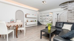 Ein modernes Wohnzimmer mit Essbereich, einer Treppe und einem schwarzen Ledersofa.