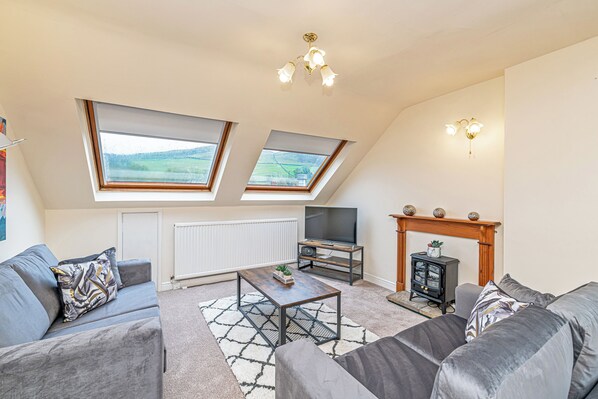 A modern living room with a sofa set, a coffee table, a TV, and a fireplace. There are skylights and a radiator visible. - Scosthrop - Bridge End Mill By Guestz (Settle)