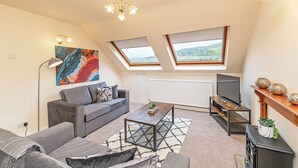 A modern living room with a grey sofa, a coffee table, and a TV stand. There are skylights and a painting on the wall. - Scosthrop - Bridge End Mill By Guestz (Settle)