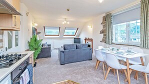 A modern kitchen with a stove, dining table, and chairs. There is a grey sofa and a potted plant in the living area. - Scosthrop - Bridge End Mill By Guestz (Settle)