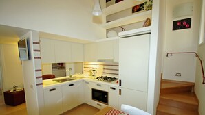 Een compacte keuken met witte kasten, een gasfornuis en een ingebouwde oven. Er is een klein zithoekje met een tafel en stoelen.