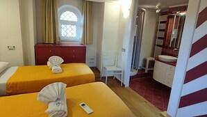 Hotelkamer met twee bedden, een rode ladekast, een raam met gordijnen, een badkamer met een rode betegelde muur en een spiegel.