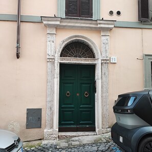 A green door with a metal ring handle, a number '21' sign above it, and a vehicle parked to the right. - HISTORICAL CENTER, TRASTEVERE, B. GESU, A/C, WiFi, 2 BEDROOMS, BATHROOM, KITCHEN (Roma)