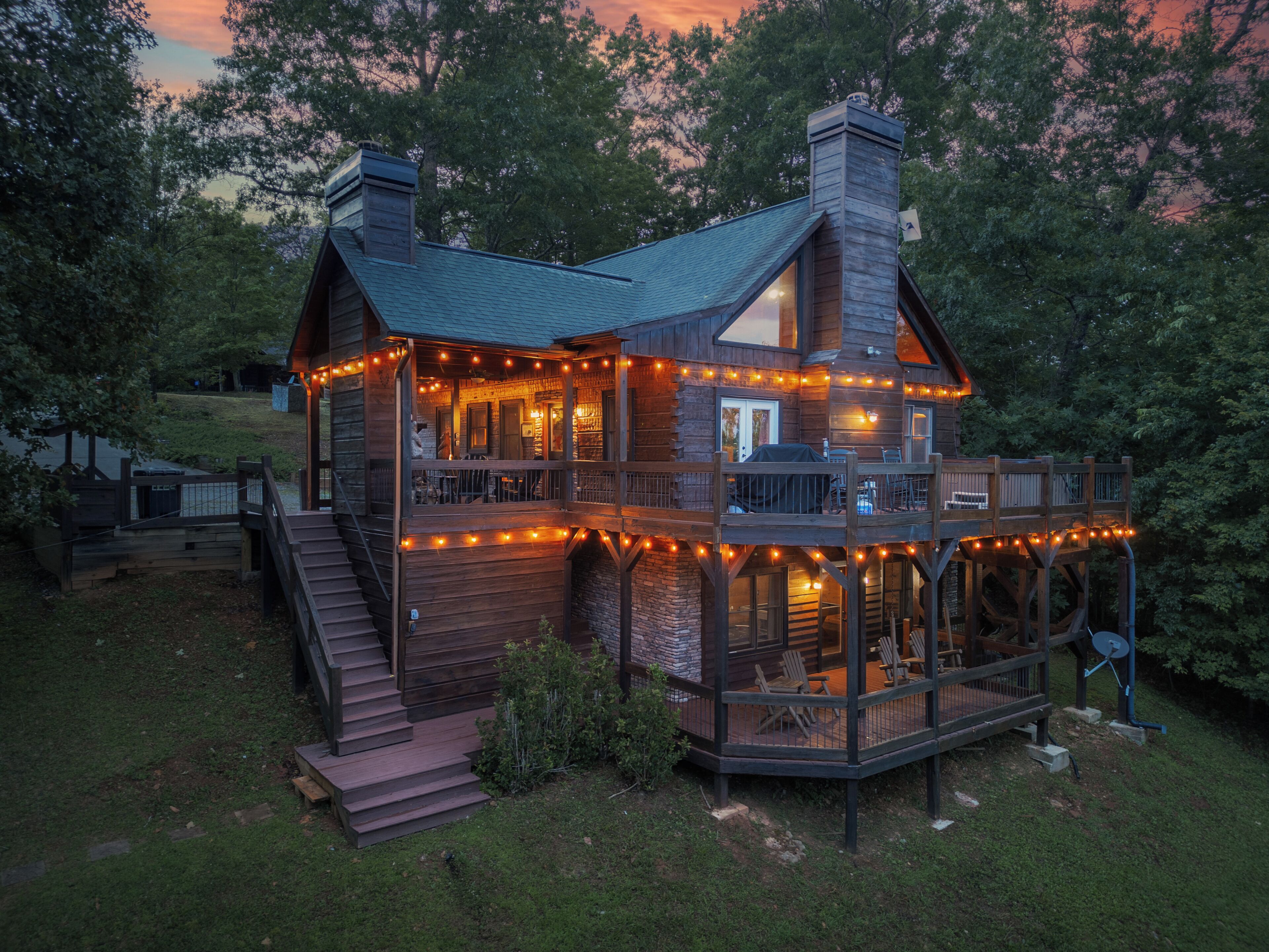 A two-story wooden cabin with a balcony, surrounded by trees.