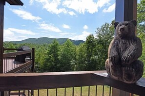 Une terrasse en bois ornée d’une statue d’ours, offrant une vue sur une chaîne de montagnes boisées.