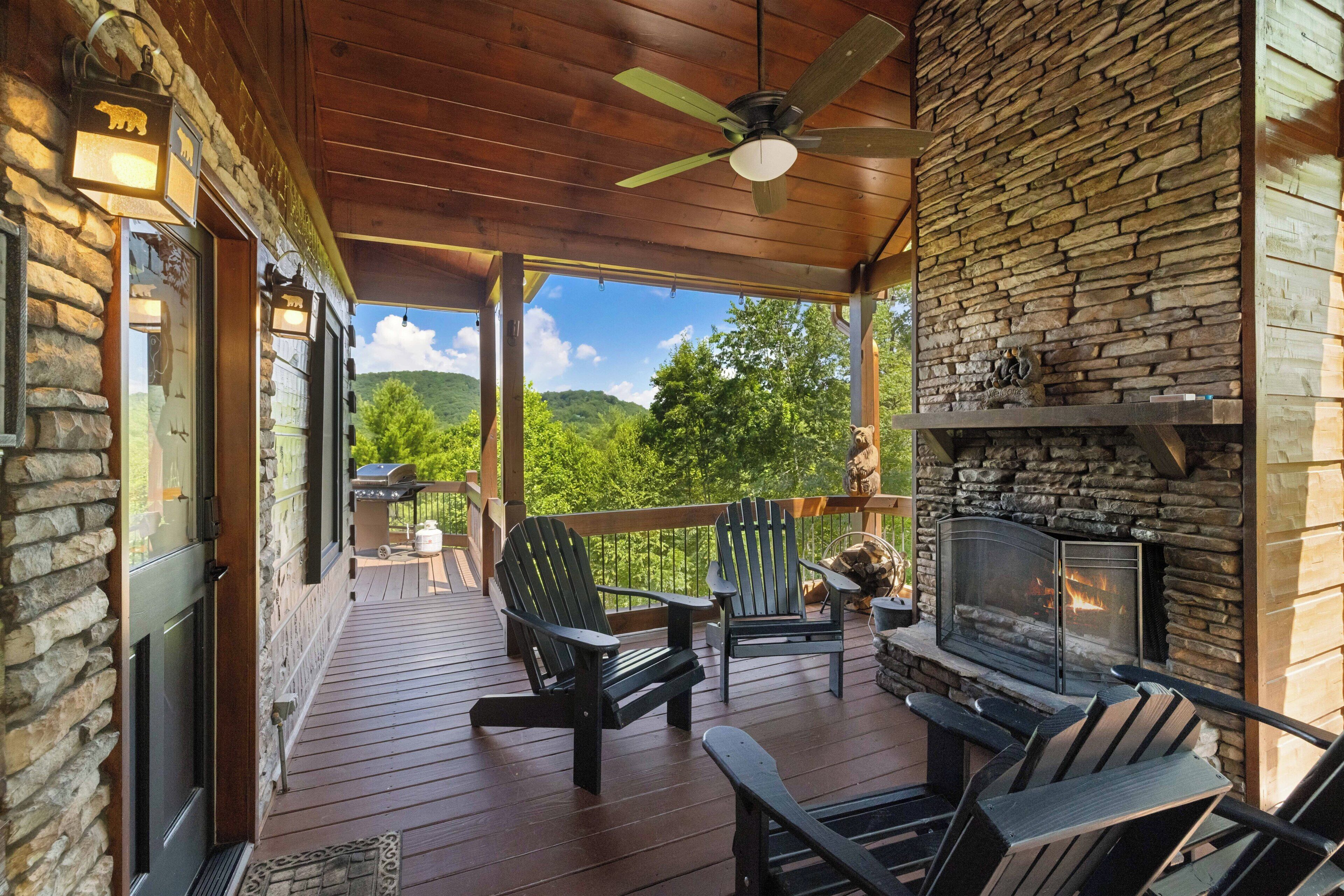 A covered outdoor deck with a stone wall, a fireplace, and outdoor seating.