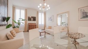 A modern living room with a glass coffee table, white sofas, a wooden side table, and a large mirror. - Santo Stefano Palace  (Venice)