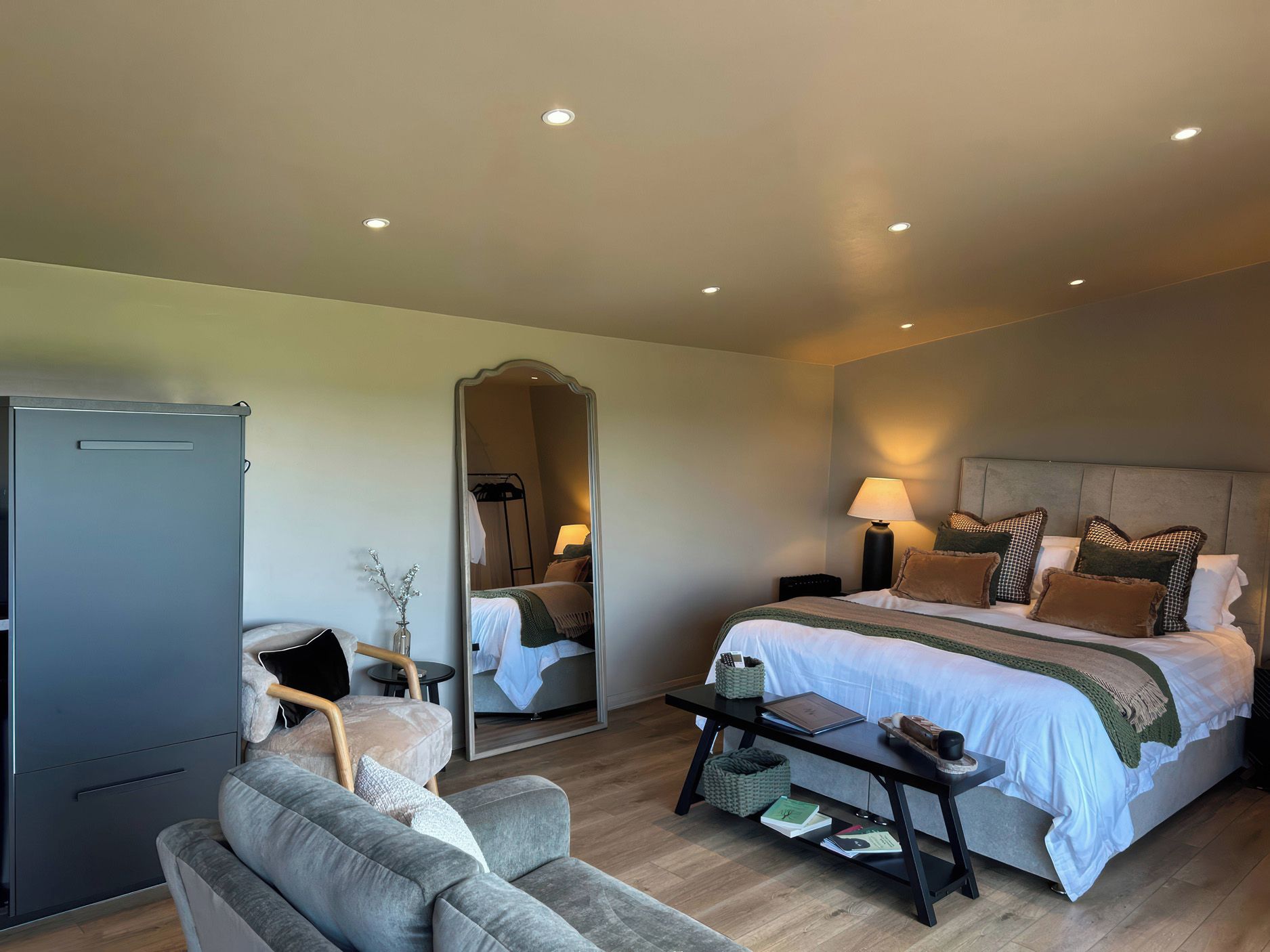 Quarto de hotel com cama, mesas de cabeceira, espelho, sofá, escrivaninha e armário.