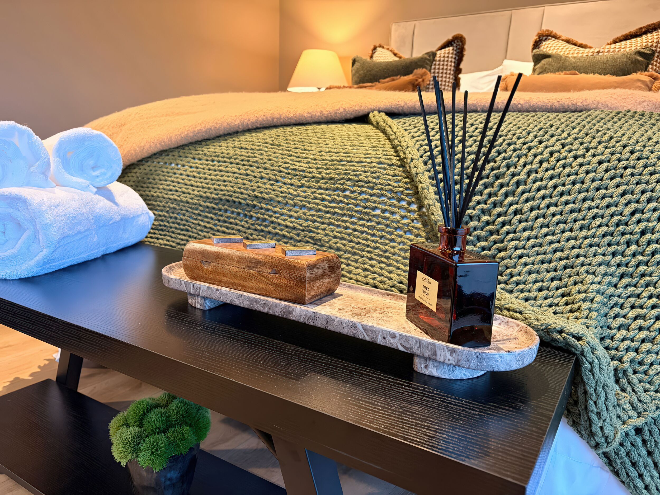 Een netjes opgeruimd nachtkastje met een houten dienblad waarop een diffuser, een klein houten doosje en een flesje essentiële olie staan.