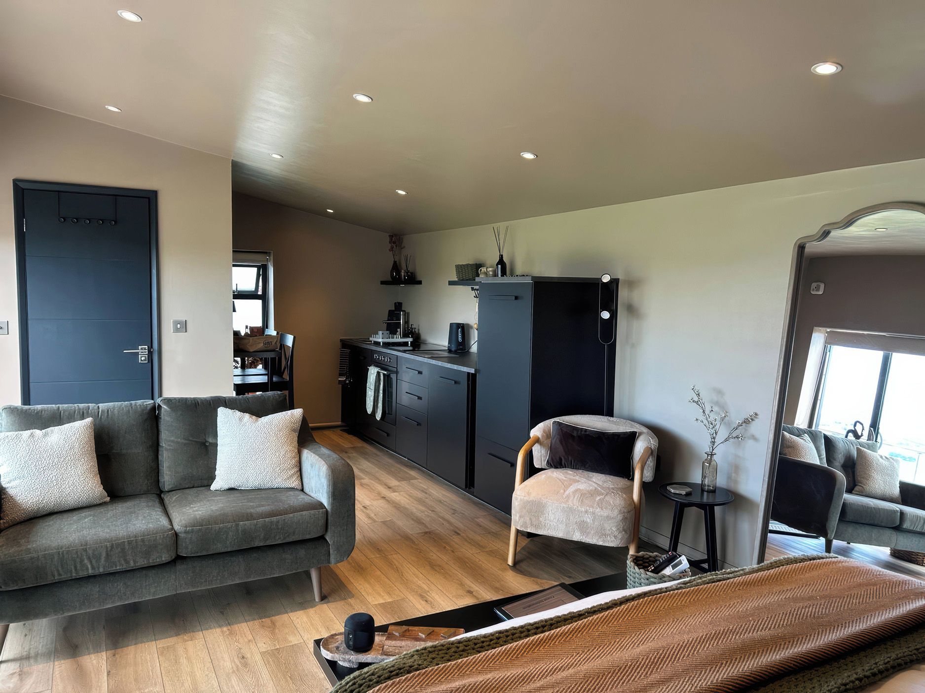 Una sala de estar moderna con un sofá, una silla, una mesita y una cocina con refrigerador y cafetera.