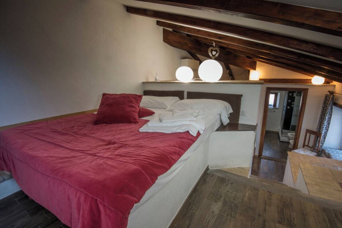 Ein Schlafzimmer mit einem Bett, einer roten Decke, einer Holzbalkendecke und einem Nachttisch.