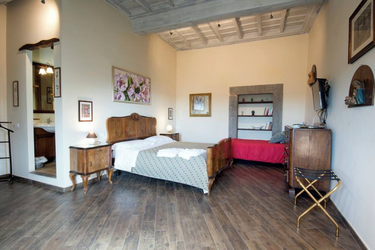Ein Schlafzimmer mit einem hölzernen Bett, einem Nachttisch, einer Kommode, einer roten Bettdecke und einem Bücherregal.