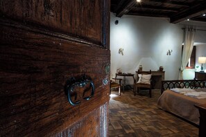 A rustic room with a wooden door, a bed, a chair, a small table, and a lamp. - Palazzo Mazzini (Bagnoregio)