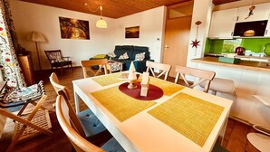 A cozy living room with a dining table, chairs, and a sofa. There is a kitchen area with a sink and a stove. - Cozy bungalow at the foot of the Wasserkuppe for up to 4 people (Dipperz)