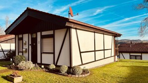 A traditional half-timbered house with a sloped roof, a satellite dish, and a well-maintained lawn. - Cozy bungalow at the foot of the Wasserkuppe for up to 4 people (Dipperz)
