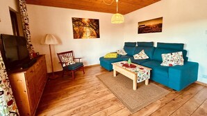 A cozy living room with a wooden ceiling, a blue sofa, a wooden coffee table, and a television on a wooden cabinet. - Cozy bungalow at the foot of the Wasserkuppe for up to 4 people (Dipperz)