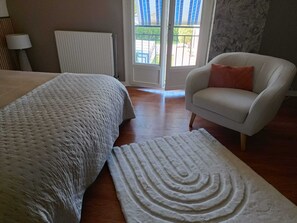 A bedroom with a bed, a chair, a radiator, and a view through a door.