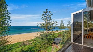 A coastal property with a wooden deck, a glass-enclosed room with a view of the beach and ocean, and a small structure with a roof. - Forresters Dunes - Upstairs (Forresters Beach)