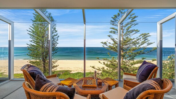 A balcony with wicker furniture, a chessboard, and a view of the beach and ocean. - Forresters Dunes - Upstairs (Forresters Beach)