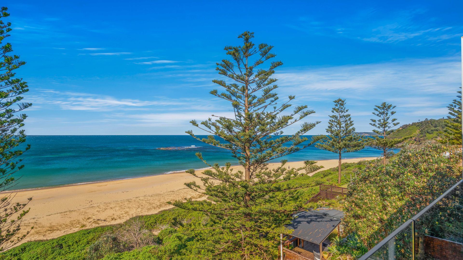 Une vue sur la plage, avec un ciel dégagé, une plage de sable et quelques arbres.