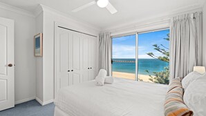 A bedroom with a large bed, a ceiling fan, and a view of the beach. - Forresters Dunes - Upstairs (Forresters Beach)