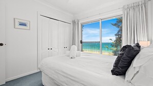 A hotel room with a large bed, a view of the sea, and a door with a picture on the wall. - Forresters Dunes - Downstairs (Forresters Beach)