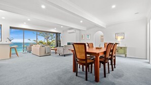 A spacious living area with a large dining table, comfortable seating, and a view of the ocean. - Forresters Dunes - Downstairs (Forresters Beach)