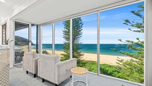 A modern room with a large sliding glass door leading to a beach view, a grey sofa, and a small wooden table. - Forresters Dunes - Downstairs (Forresters Beach)