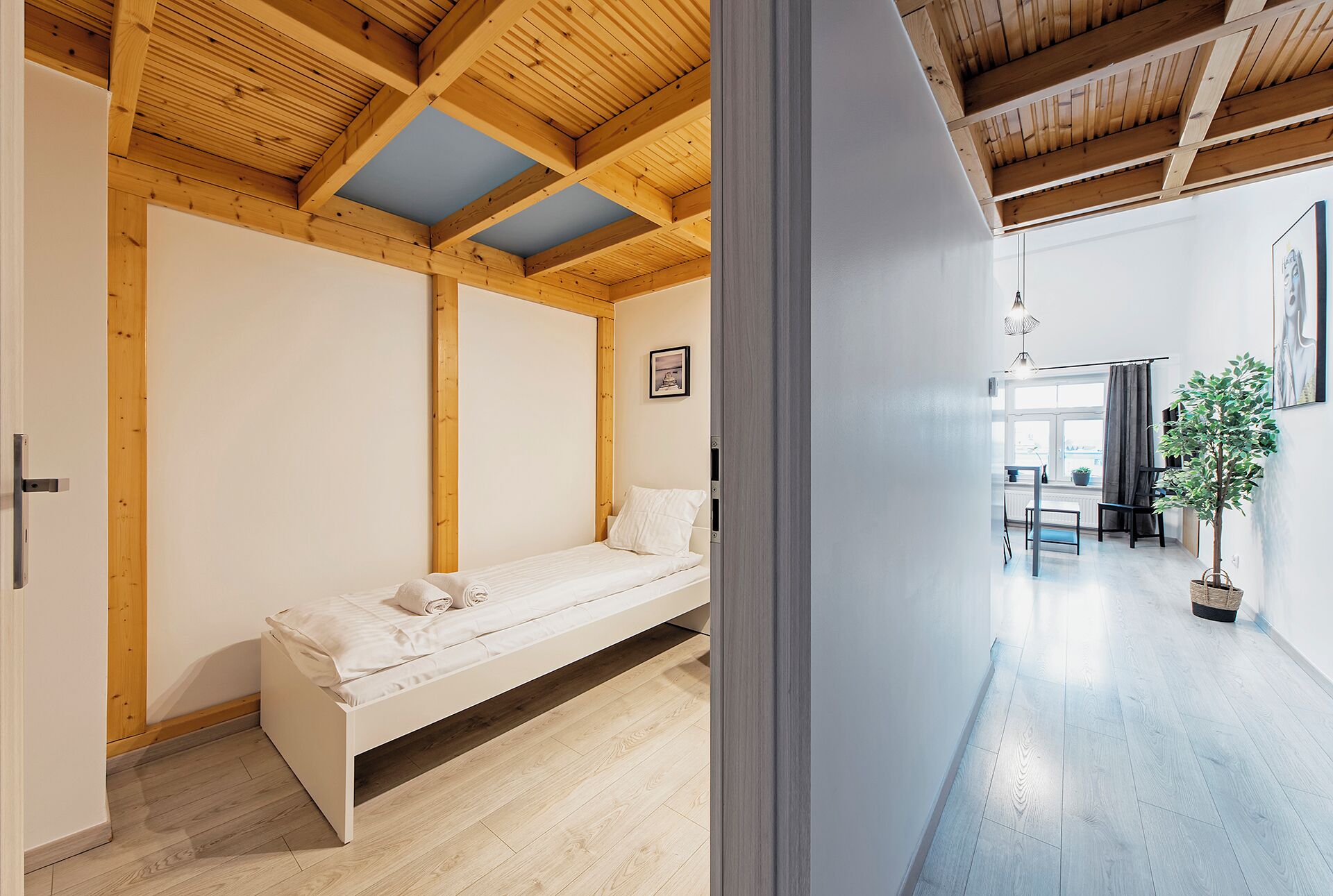 A minimalist bedroom with a wooden ceiling, a single bed, a small bedside table, and a window with a view.