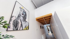 Ein modernes Interieur mit einem großen, abstrakten Gemälde an der Wand, einem Holzbalken an der Decke und Blick in einen Raum mit einer Treppe.
