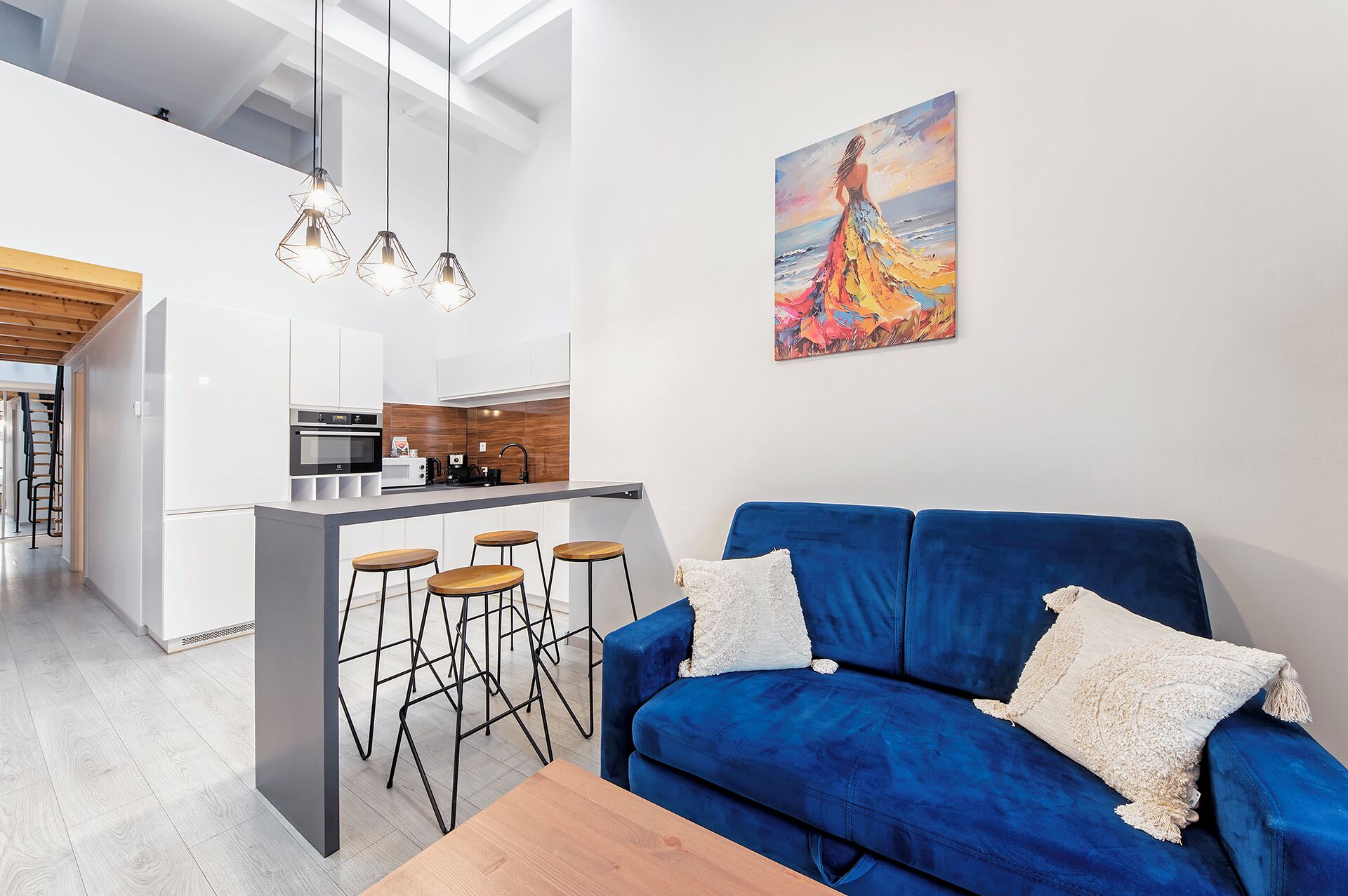 Ein moderner Wohnbereich mit einem blauen Sofa, Holzschemeln und einer Küchenzeile.