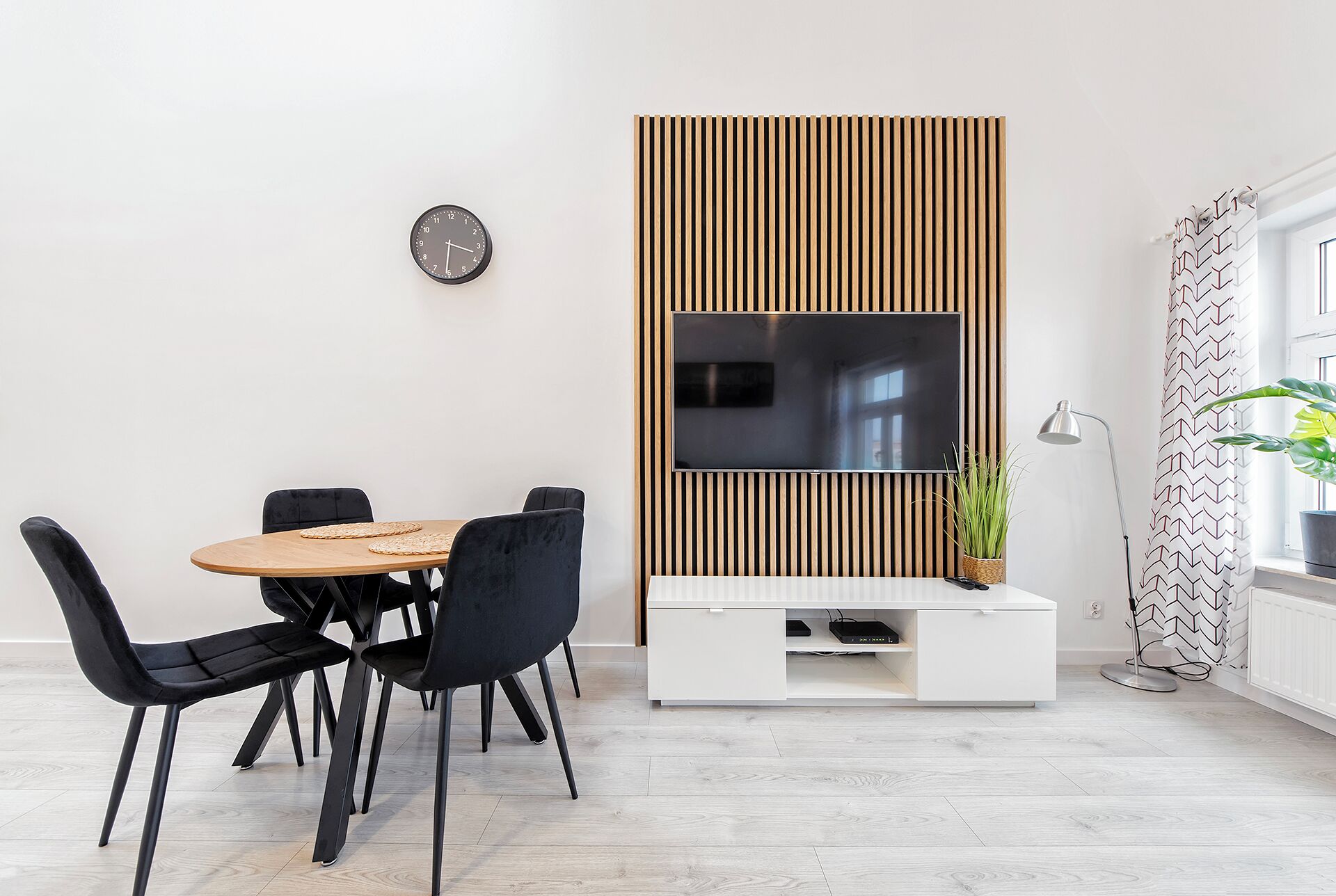 En moderne stue med en væg af trælameller, et fladskærms-tv, et spisebord med stole og en stueplante.