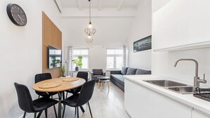 Eine moderne Küche mit Spüle, ein Essbereich mit Tisch und Stühlen sowie ein Wohnbereich mit Sofa und Fernseher.