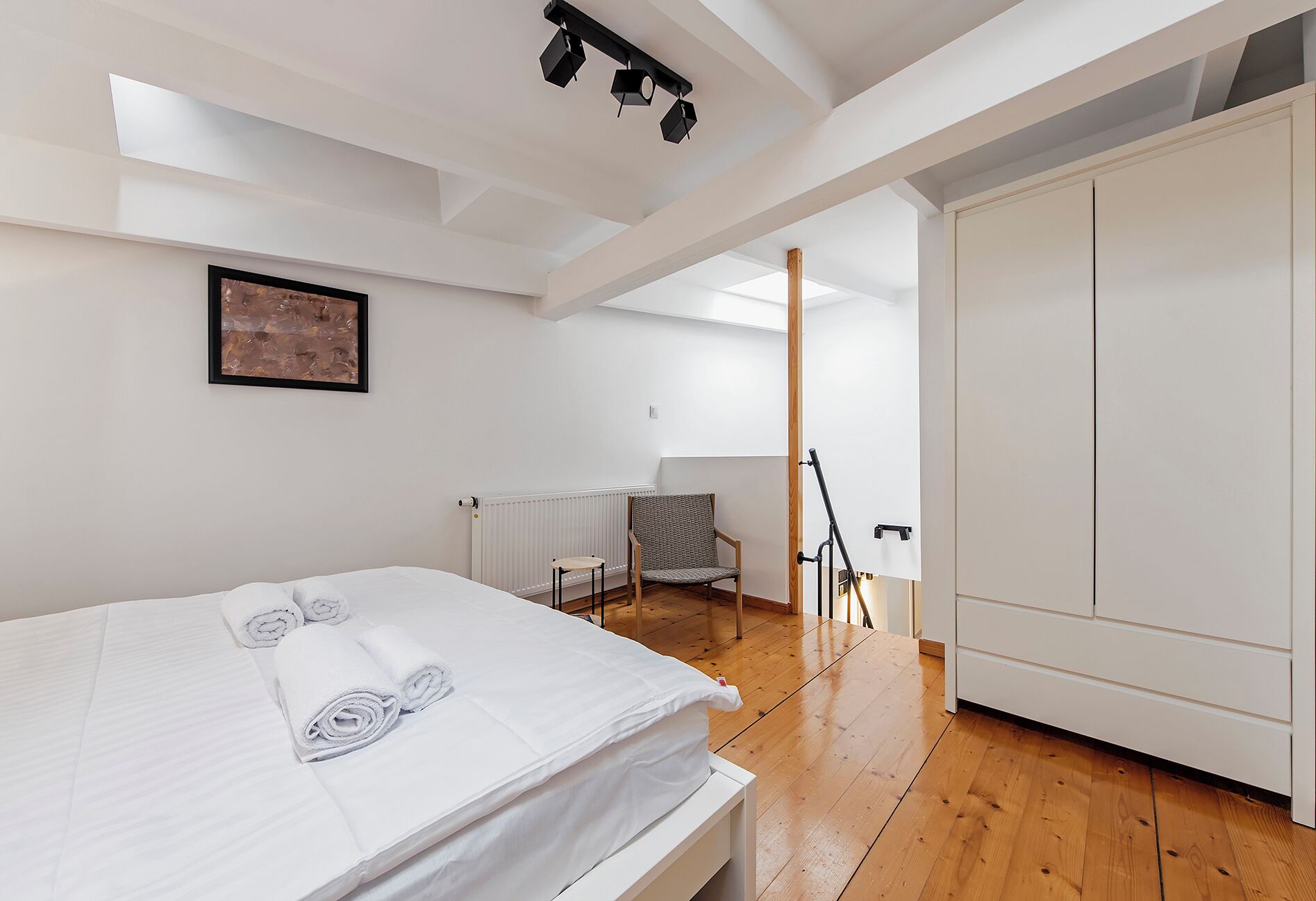 Ein modernes Schlafzimmer mit einem großen Bett, einem Sessel, einer Heizung und einem Kleiderschrank.