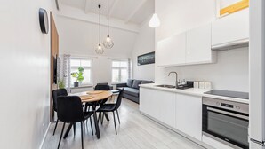 Eine moderne Küche mit weißen Schränken, einem eingebauten Backofen und einem Essbereich mit Holztisch und schwarzen Stühlen.