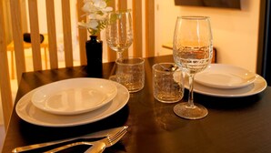 A dining table set with plates, glasses, and cutlery, with a vase of flowers and a wall-mounted air conditioner in the background. - Éveil en blanc - Private Jacuzzi & cotton comfort (Verdun)