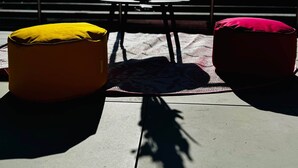 Un espace extérieur ensoleillé, aménagé avec une table, deux coussins et un vase rempli de fleurs.