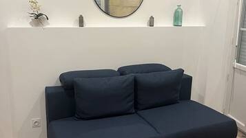 Een moderne woonkamer met een donkerblauwe bank, een ronde spiegel aan de muur, en een klein plankje met decoratieve objecten.