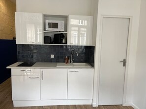 A kitchen with white cabinets, a microwave, a sink, and a door. - Appartement climatisé au cœur de Bordeaux (Bordeaux)